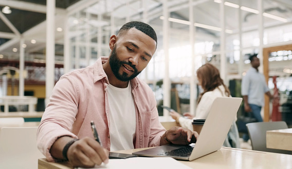 A student studying on his laptop and taking notes