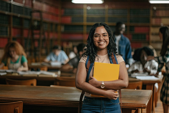 A student standing in a study hall smiling at the camera